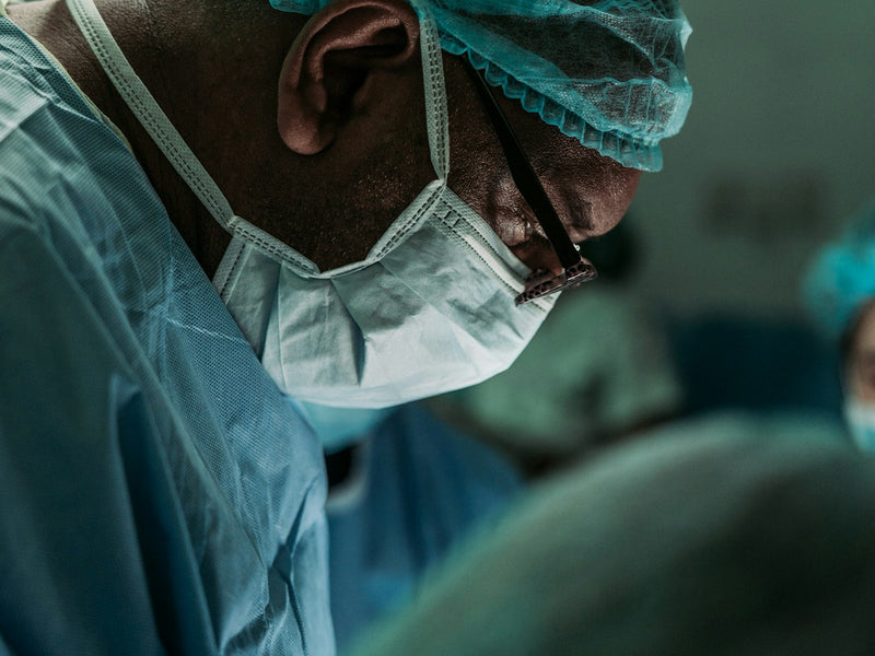 A surgeon in cap and mask, head down over the operating table
